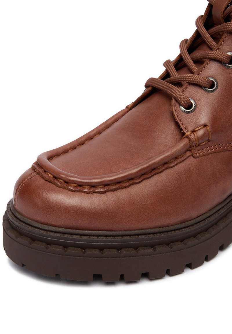 Stivale moc toe in pelle marrone con suola in gomma nera spessa e lacci marroni rotondi passati attraverso occhielli in metallo.