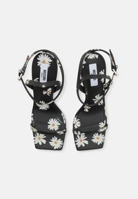 Fekete platform szandálok virágos margaréta mintával. Állítható bokapántokkal rendelkezik, és fényes felülettel bír a felső anyagon.