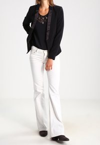 Blazer nero con revers in satin, indossato sopra un top scuro con ricami. Abbinato a jeans bianchi a palazzo e stivaletti neri.