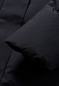 Chaqueta de plumas negra con un acabado mate suave, con una manga voluminosa y una silueta elegante, diseñada para ofrecer aislamiento y comodidad.