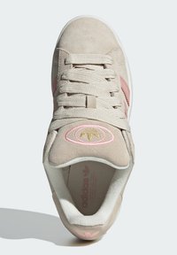 Beige suede sneaker with pink accents, round logo with golden detail, flat laces, and white rubber sole. Textured interior lining.