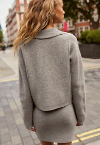 Conjunto de chaqueta y vestido de mezcla de lana gris con un cuello acanalado y mangas largas, que presenta un diseño en capas y una textura suave.