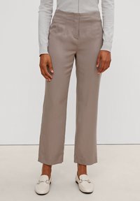 Pantalons larges beiges avec une texture lisse, dotés de plis sur le devant et d'une taille haute. Portés avec un haut à manches longues gris clair et des mocassins blancs.