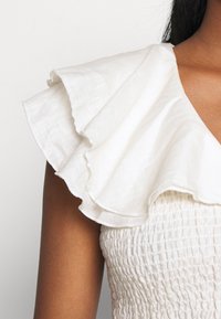 Vestido branco de linho com mangas repuxadas e corpete texturizado com franzido. O tecido é leve, com um acabamento suave e natural.