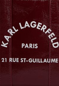 Burgundy leather bag features embossed white text: "KARL LAGERFELD," "PARIS," and "21 RUE ST-GUILLAUME," with a smooth texture.