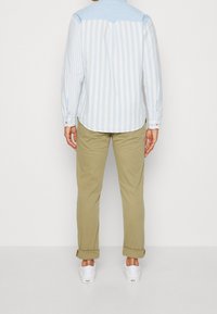 Vaaleansininen ja valkoinen raidallinen paita, jossa on chambray-olka, nappi- ja hihansuut, yhdistettynä khaki-housuihin ja valkoisiin kenkiin.