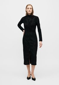 Fekete, hosszú ujjú ruha magas nyakú kivitelben, texturált mintával, elöl hasítékkal és slim fit szabással, puha anyagból készült, és a lábszár közepéig ér.