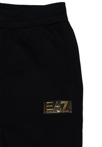 Pantaloni sportivi neri con una cintura testurizzata, dotati di un patch con logo dorato EA7 Emporio Armani sulla coscia destra.