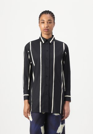 Camicia nera con bottoni, strisce verticali bianche, maniche lunghe e colletto classico; realizzata in un tessuto morbido con una vestibilità comoda.
