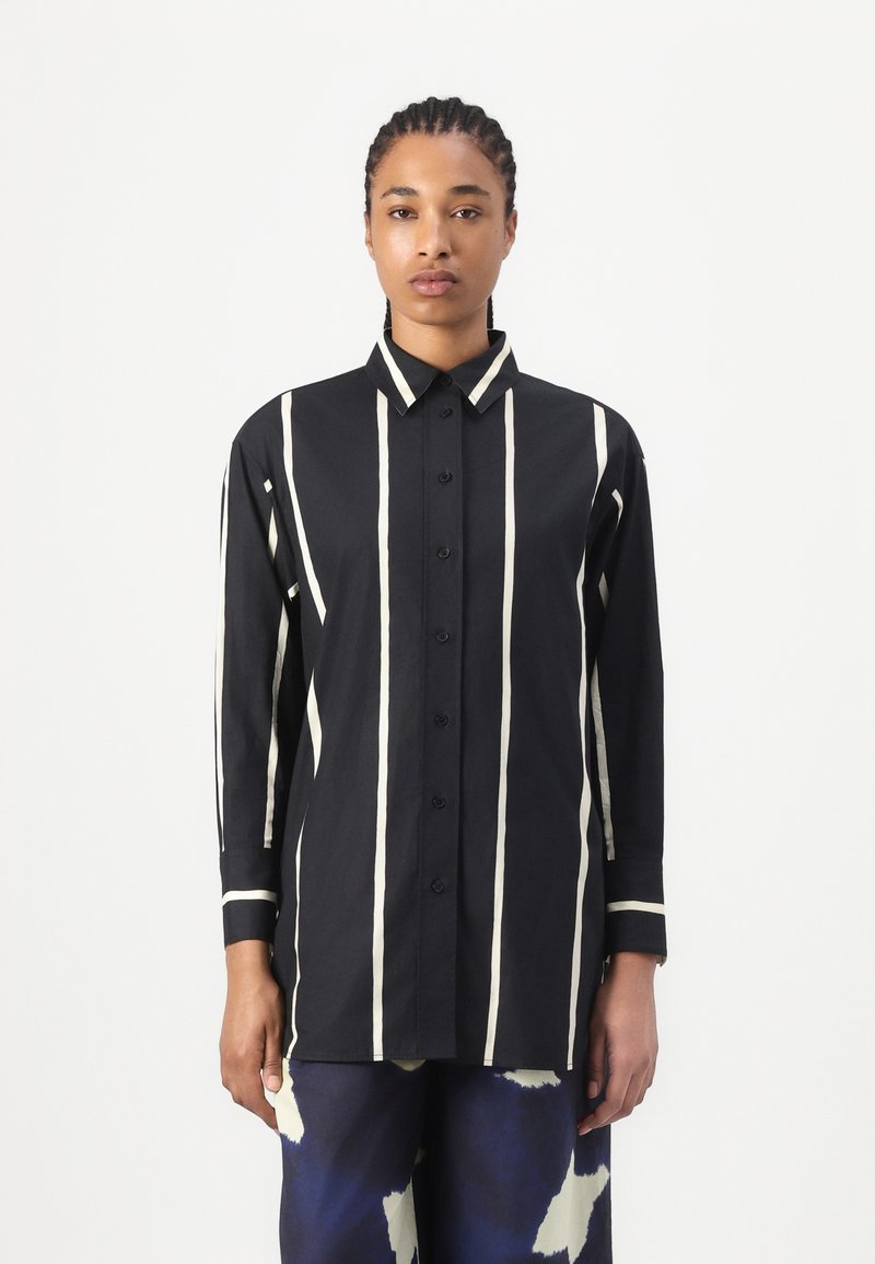 Black button-up shirt with white vertical stripes, long sleeves, and a classic collar; made of smooth fabric with a relaxed fit.