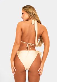 Nude bikini met halternekkraag en strikbandjes. Hooggesneden broekje met zijstrikjes. Glad, glanzend stof. Ontwerp met minimale bedekking.