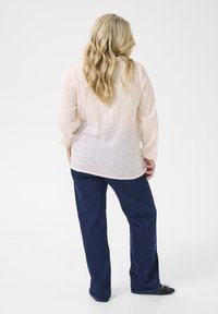 Light pink, long-sleeve blouse with decorative eyelet pattern, paired with dark blue wide-leg jeans and black shoes. Casual, relaxed fit.