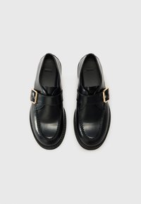 Black leather loafers with a smooth finish, featuring a strap and gold-tone buckle. Rounded toe and contrast stitching detail.
