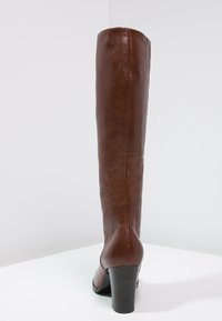 Botte haute jusqu'au genou en cuir marron avec une texture lisse, un bout arrondi et un talon épais. Présente une couture verticale simple à l'arrière.