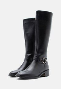 Kelnų ilgio juodi odiniai batai su smailiu priekiniu, mažu blokiniu kulnu, šonine užtrauktuku ir dekoratyvine juosta su auksinės spalvos apvaliu akcentu.