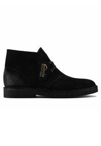 Black suede desert boots featuring a rounded toe, simple lace-up design, and a branded tag, with a flat rubber sole and stitched accent.