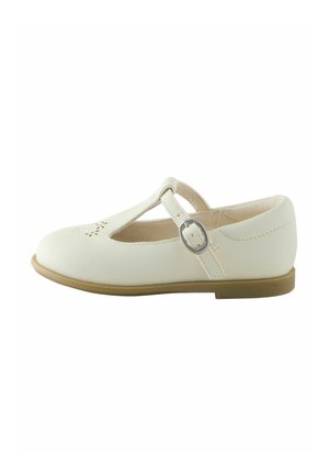White leather Mary Jane shoe with a rounded toe, T-strap design, ankle buckle, and cut-out flower pattern on the toe. Flat tan sole.