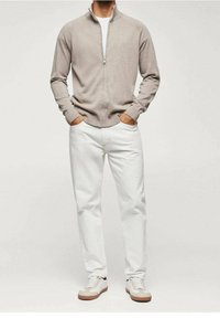 Maglione beige con zip, t-shirt bianca sotto, jeans bianchi e sneakers bianche con dettagli beige. Tessuto morbido, vestibilità casual.