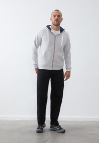 Grijze hoodie met witte trekkoorden en een contrasterende marineblauwe binnenvoering, gecombineerd met zwarte broek en grijze sportschoenen. Eenvoudig ontwerp, casual pasvorm.