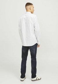 Cămașă cu mânecă lungă, albă și albastră deschis cu dungi, cu manșete cu nasturi, combinată cu blugi negri din denim și adidași albi cu accente negre.