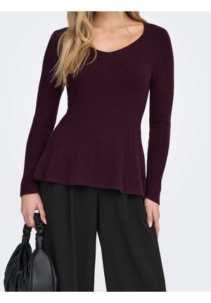 Mujer con un suéter de canalé color ciruela con mangas largas y bajo acampanado, pantalones negros de pierna ancha y sosteniendo un bolso de cuero negro.