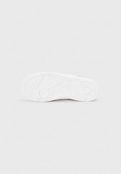 Vit sneakersåld med texturerad gummi, som har en slät yta, spår för grepp och en präglad logotyp på sidan.