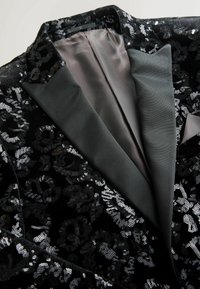 Zwarte pailletten blazer met een gladde satijnen revers en grijze satijnen voering. Close-up van de gedetailleerde patronen en texturen aan de buitenkant.