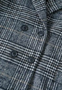 Wollmischung Jacke mit einem Hahnentrittmuster. Vorwiegend marineblau und grau mit schwarzen Knöpfen und strukturiertem Stoff. Doppelreiher-Design.