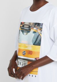 Weißes, übergroßes T-Shirt mit einem großen Fotodruck eines gelben Taxis mit einem "DKNY"-Schild, das eine Stadtlandschaft und Details des Nummernschilds zeigt.