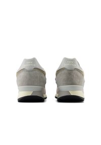 Sneaker in suede e pelle grigia con una forma arrotondata, caratterizzata da accenti bianchi e suola in gomma nera. Logo "New Balance" sul tallone.