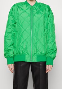 Gevoerd groen bomberjack van glanzend materiaal, met een ritsluiting, ribgebreide manchetten en tailleband; diamantpatroon over het hele jack.