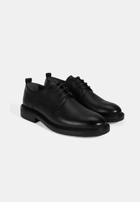Zwarte leren schoenen met een gestructureerde afwerking, ronde neus en vetersluiting. Heeft een lage hak en een soepele, duurzame zool.