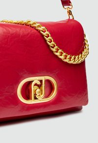 Sac à main en cuir rouge avec une finition texturée, une bandoulière en chaîne dorée et un fermoir doré distinctif avec des lettres entrelacées.