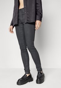 Vaqueros negros de corte slim, fabricados en denim, con una textura suave. Combinados con unos zapatos negros de plataforma y una camisa oscura de botones.