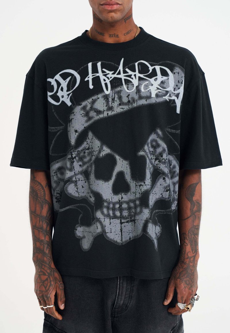 Camiseta de gran tamaño en negro con un gráfico de una calavera gris con huesos cruzados y texto en estilo graffiti en la parte frontal. Material de algodón, mangas cortas.