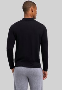 Czarna koszulka polo z długim rękawem o prążkowanej fakturze, z prążkowanym kołnierzykiem i szwami na ramionach, zestawiona z szarymi dresami.