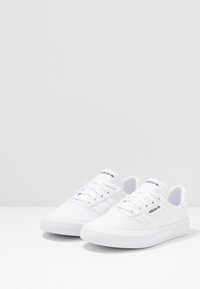 Białe tenisówki z płótna o teksturowanym wykończeniu, z niskim profilem, wiązane sznurowadłami, z delikatnym logo na języku i boku.
