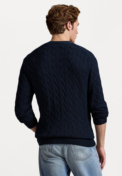 Ναυτικό πουλόβερ με πλέξη καλωδίου και υφασμάτινο σχέδιο, στρογγυλή λαιμόκοψη και ribbed μανίκια και τελείωμα. Φορώντας το με ανοιχτό μπλε τζιν.