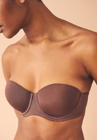 Soutien-gorge marron sans bretelles en tissu lisse avec bonnets moulés et armatures. Le design présente des coutures nettes et une finition sans couture.