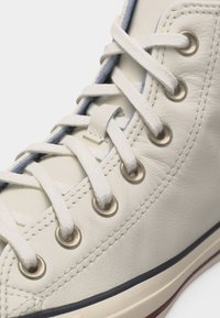 Κοντινό πλάνο λευκού δερμάτινου αθλητικού παπουτσιού με λευκά κορδόνια περασμένα μέσα από μεταλλικά ρέλια και λεπτομερή ραφή κατά μήκος της πλευράς.