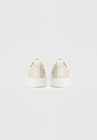 Μπεζ αθλητικά παπούτσια με ανάγλυφο σχέδιο, που διαθέτουν διακοσμητικό επάνω μέρος, λευκή σόλα και θηλιές στο πίσω μέρος για εύκολη φορεσιά.