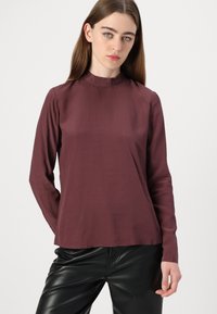 Long-sleeve maroon top with a high neckline, made of smooth fabric. Features a relaxed fit, subtly curved hem, and no visible patterns or hardware.