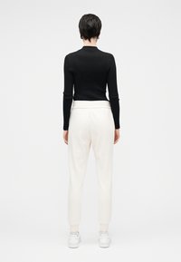 Μαύρο ριμπ μπλουζάκι με μακριά μανίκια συνδυασμένο με λευκή κωνική φόρμα και λευκά αθλητικά παπούτσια. Απλός σχεδιασμός, απαλό ύφασμα και ελαστική μέση.