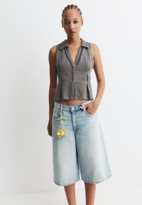 Grau geripptes ärmelloses Oberteil mit Kragen, kombiniert mit hellblauen Denim-Culottes, die einen Blumen-Schlüsselanhänger an der Gürtelschlaufe haben.
