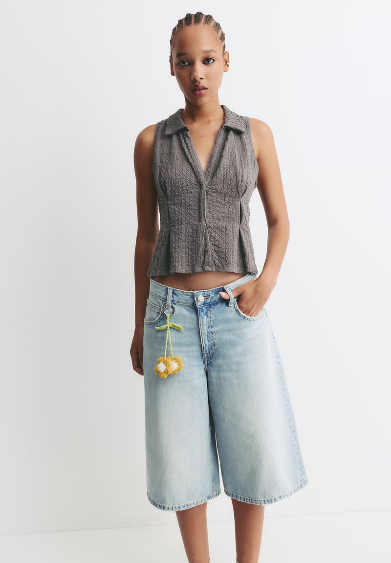 Grau geripptes ärmelloses Oberteil mit Kragen, kombiniert mit hellblauen Denim-Culottes, die einen Blumen-Schlüsselanhänger an der Gürtelschlaufe haben.