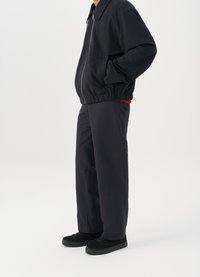 Μαύρο bomber jacket με φερμουάρ μπροστά, ελαστικούς σφιγκτήρες και στρίφωμα; συνδυασμένο με σκούρες tapered παντελόνες και μαύρα αθλητικά παπούτσια. Απλός, καθαρός σχεδιασμός.