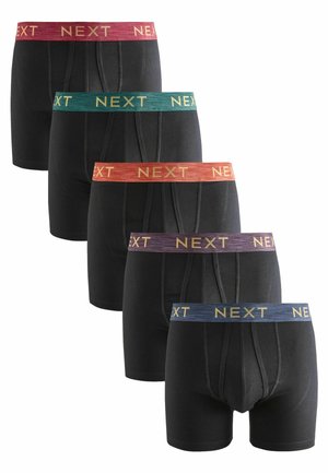 Bóxer negro con cinturillas elásticas de varios colores. Cada cinturilla presenta la palabra "NEXT" en letras doradas. Varias parejas exhibidas en una fila.
