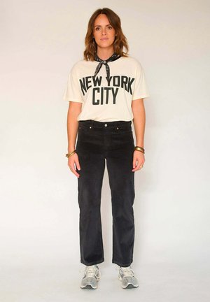 T-shirt en coton crème avec un imprimé noir audacieux "NEW YORK CITY", associé à un pantalon en velours côtelé noir et des baskets de sport grises. Accents de bandana.