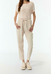 Top leggero in maglia con macchie rosa, abbinato a pantaloni beige con cordino in vita. La modella indossa sneakers platform color nocciola con dettagli chiari.