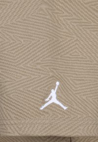 Bežinės tekstūros audinys su zigzaginiu raštu; apatinėje dalyje yra baltas išsiuvinėtas Jumpman logotipas.